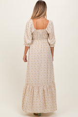 woman wearing a beige floral maternity maxi dress with puff sleeves and a ruffled hem, shown from the back