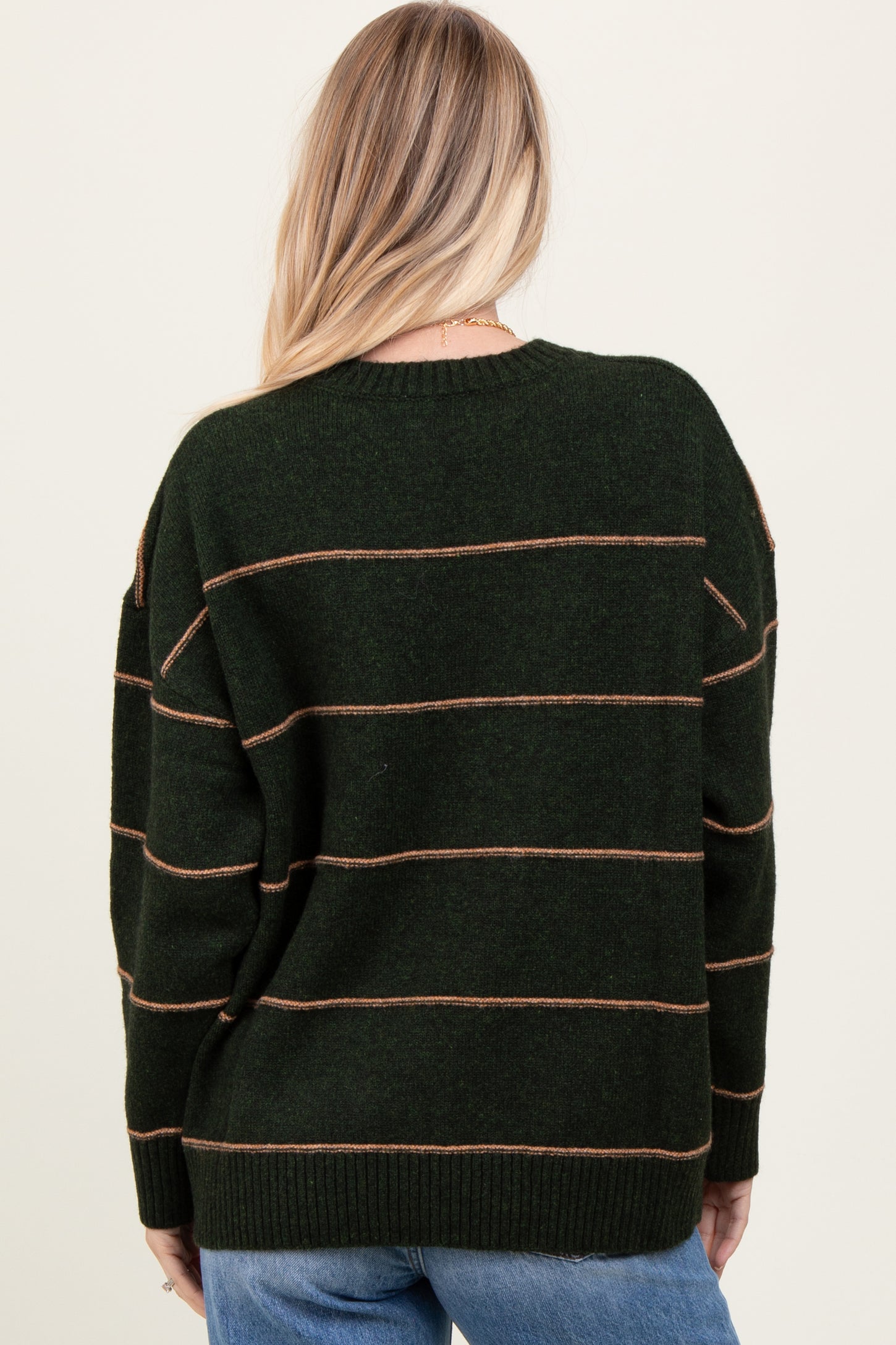woman wearing a dark green oversized sweater with brown stripes, showing the back view