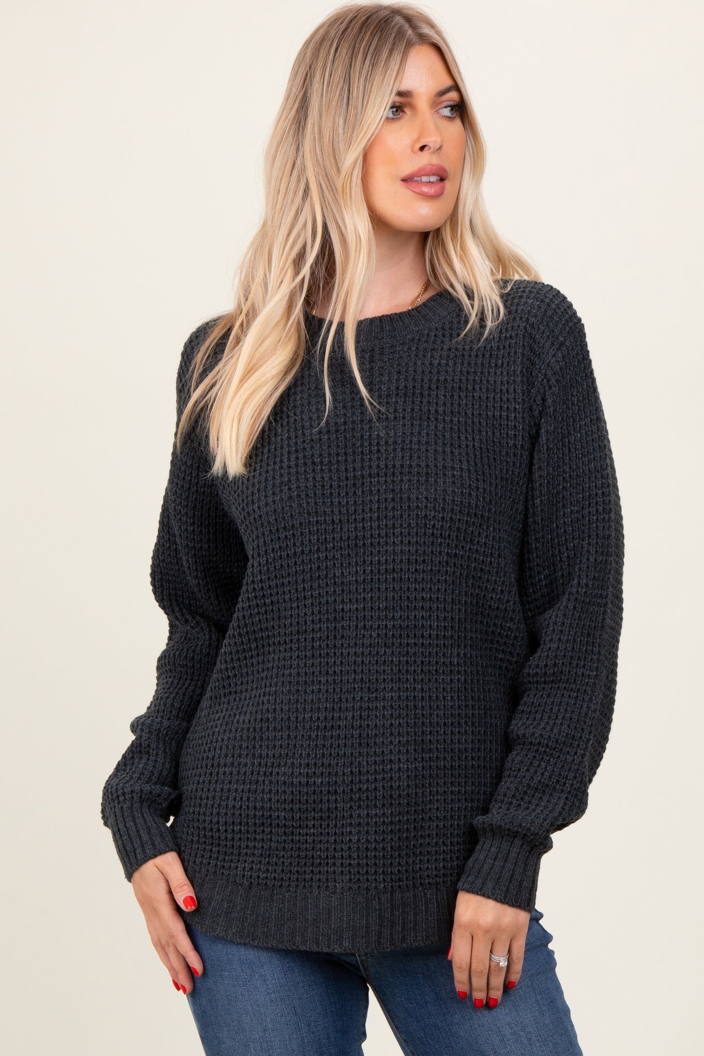 woman wearing a dark gray chunky knit sweater with long sleeves and a relaxed fit, styled with blue jeans