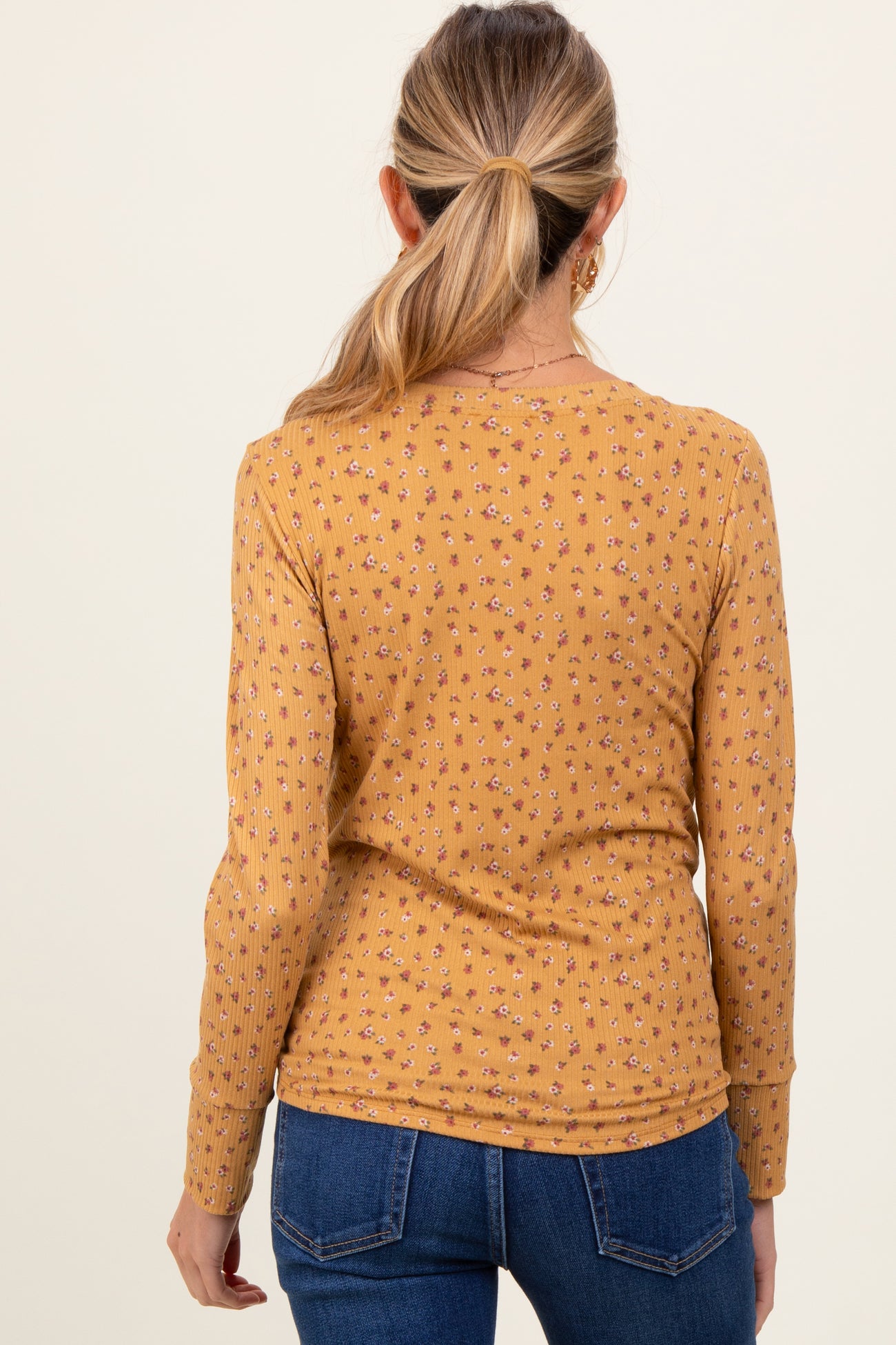 woman wearing a mustard yellow maternity top with a floral pattern and long sleeves, viewed from the back