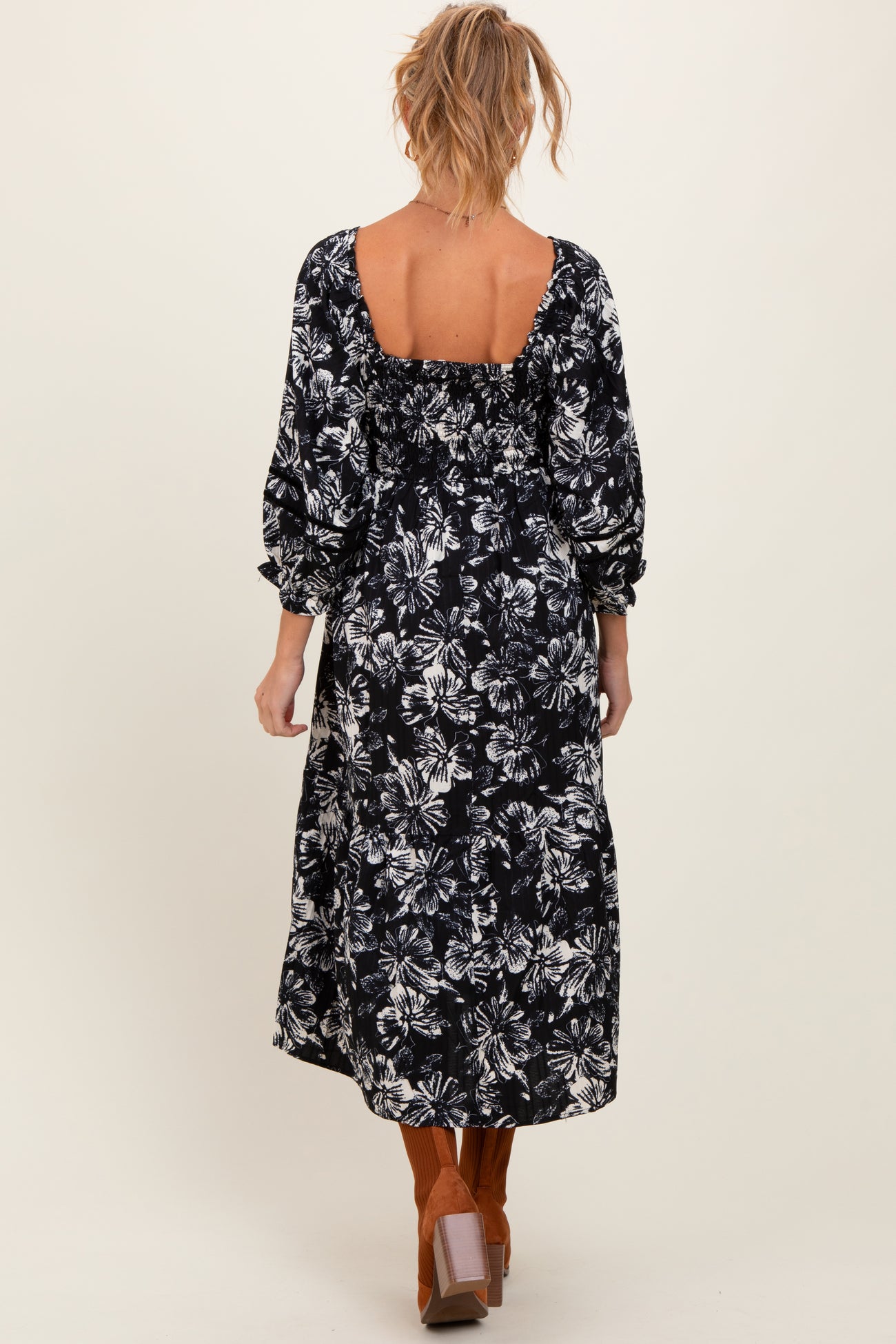 woman wearing a black floral print maternity maxi dress with puffy sleeves and an open back