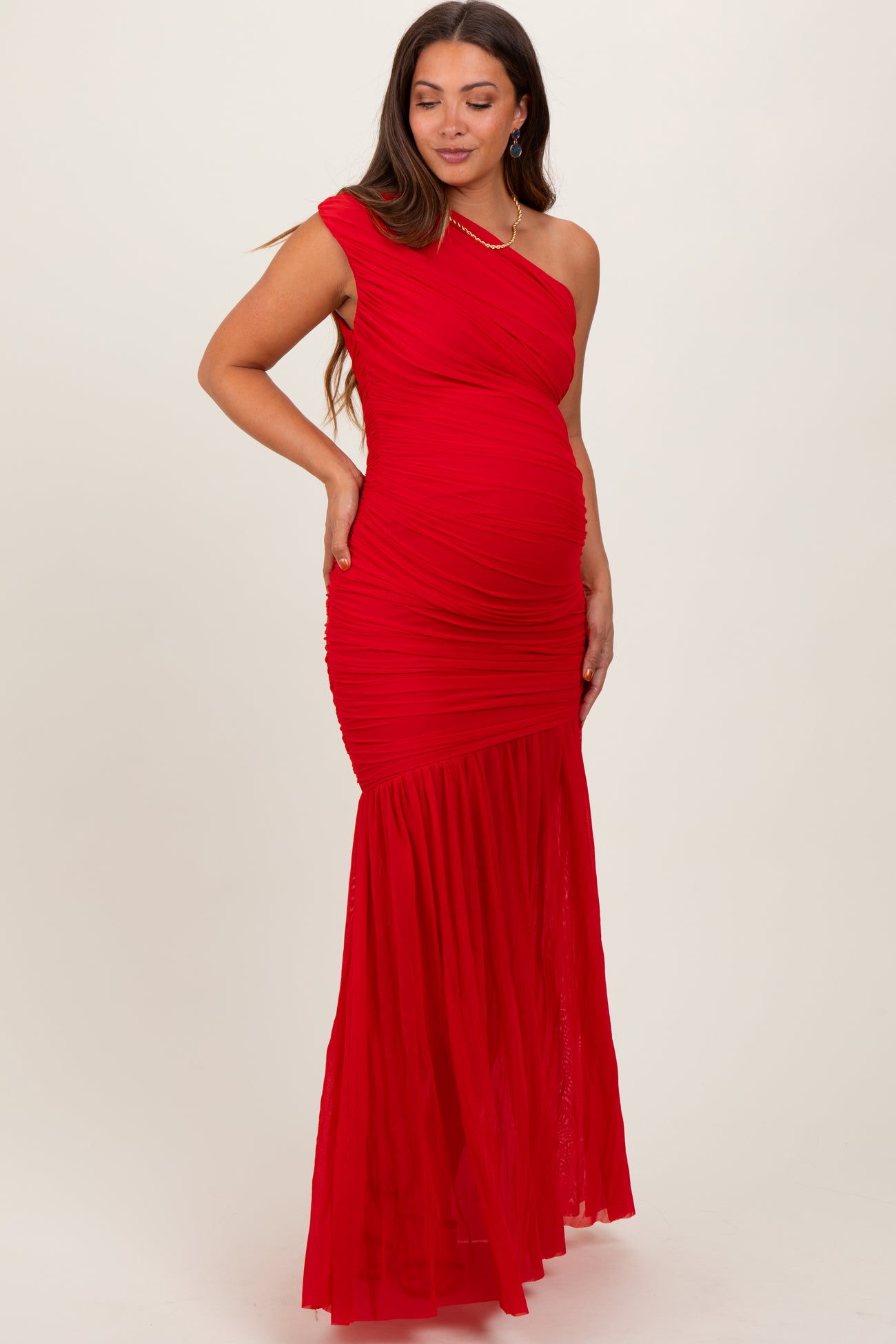 woman wearing a red one-shoulder maternity dress with ruching and a flowing skirt, showcasing her baby bump