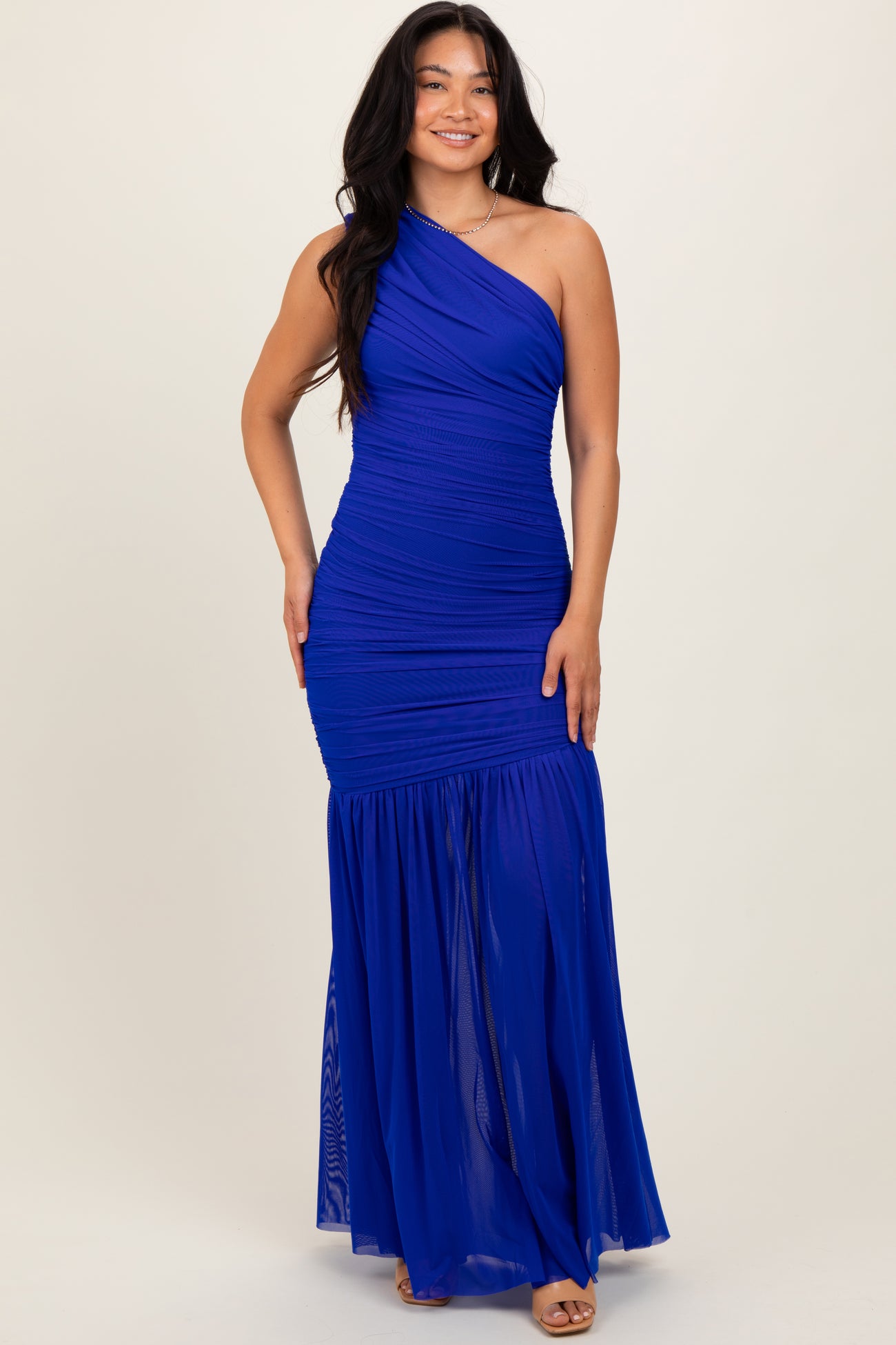 woman wearing a royal blue one-shoulder evening gown with a fitted bodice and flowy ruffled skirt