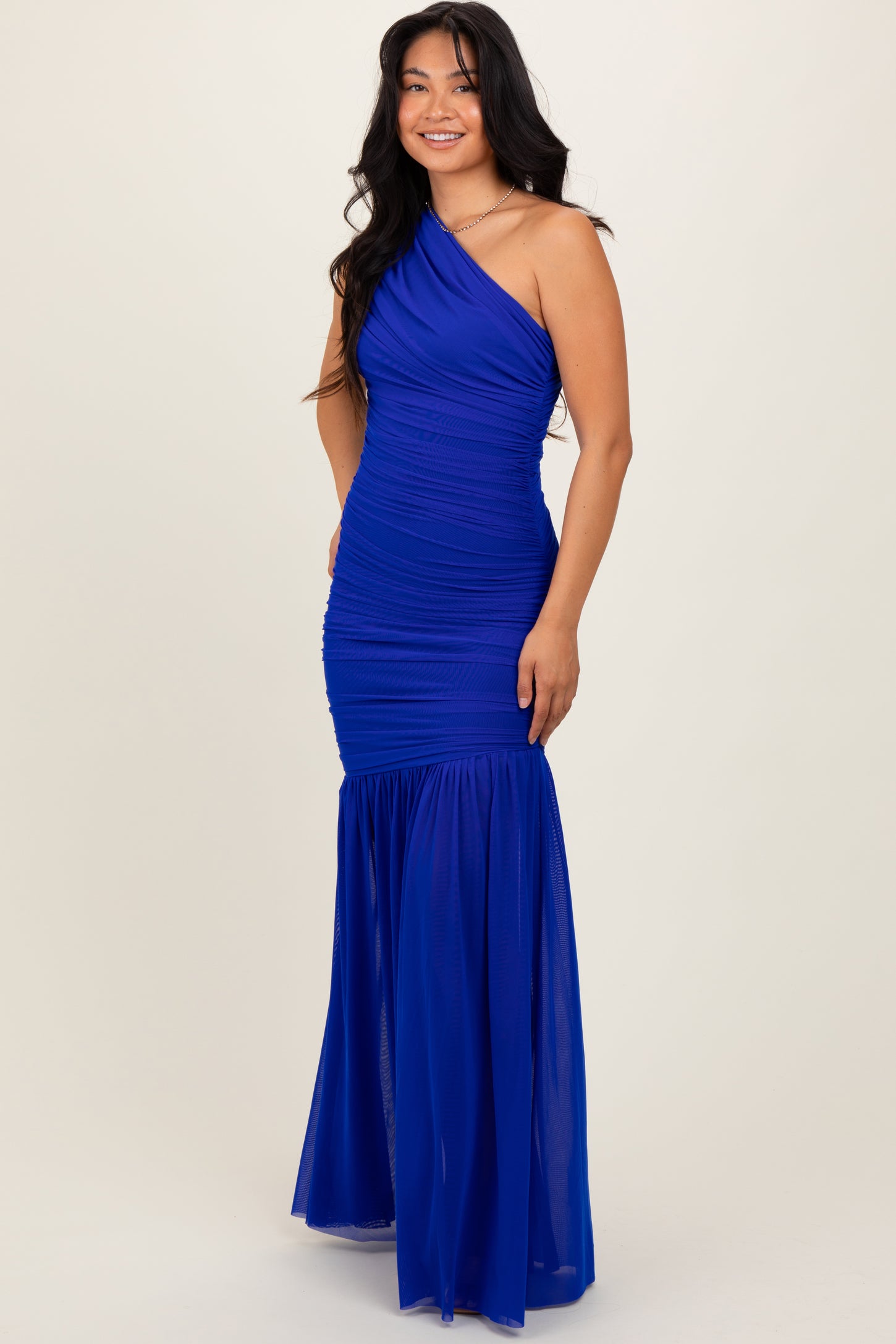 woman wearing a royal blue one-shoulder mermaid gown with ruched detailing and a flowing skirt