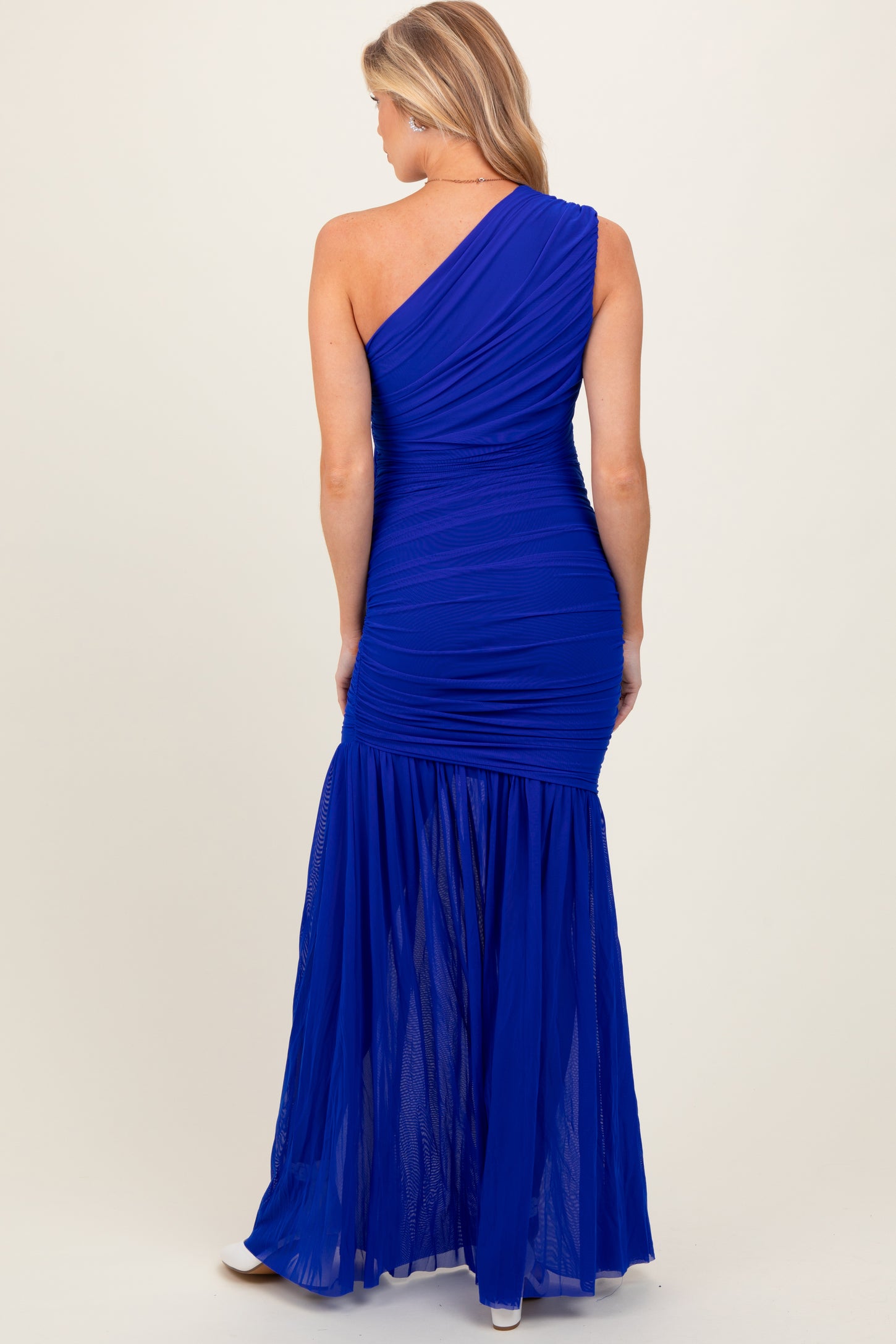 woman wearing a royal blue one-shoulder maternity dress with ruched detailing and a flowy skirt, showcasing her baby bump from the back