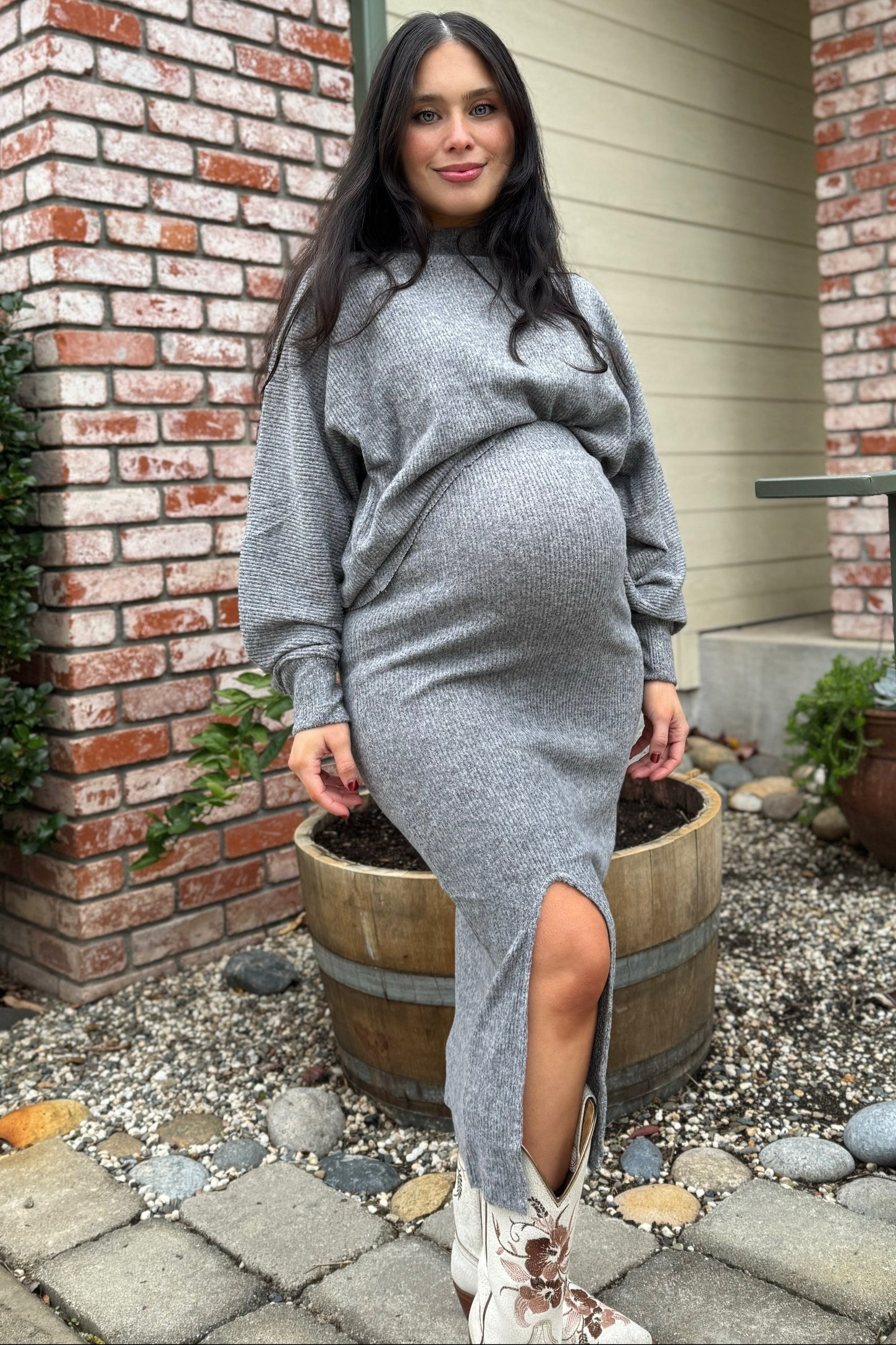 woman wearing a gray knitted maternity dress with a side slit, showcasing her baby bump, paired with white cowboy boots