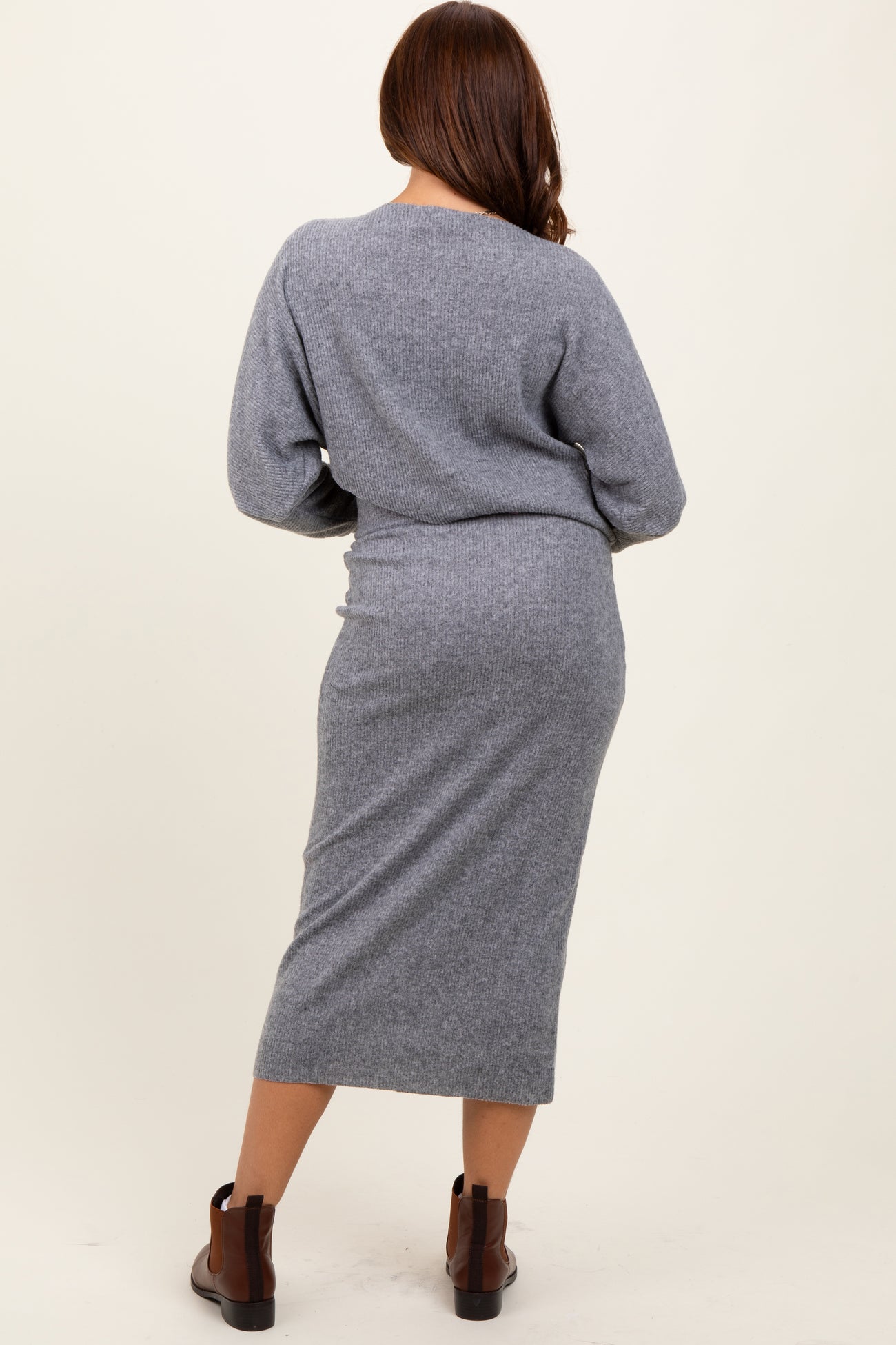 woman wearing a gray knitted long sleeve dress with a fitted silhouette and mid-calf length, seen from the back