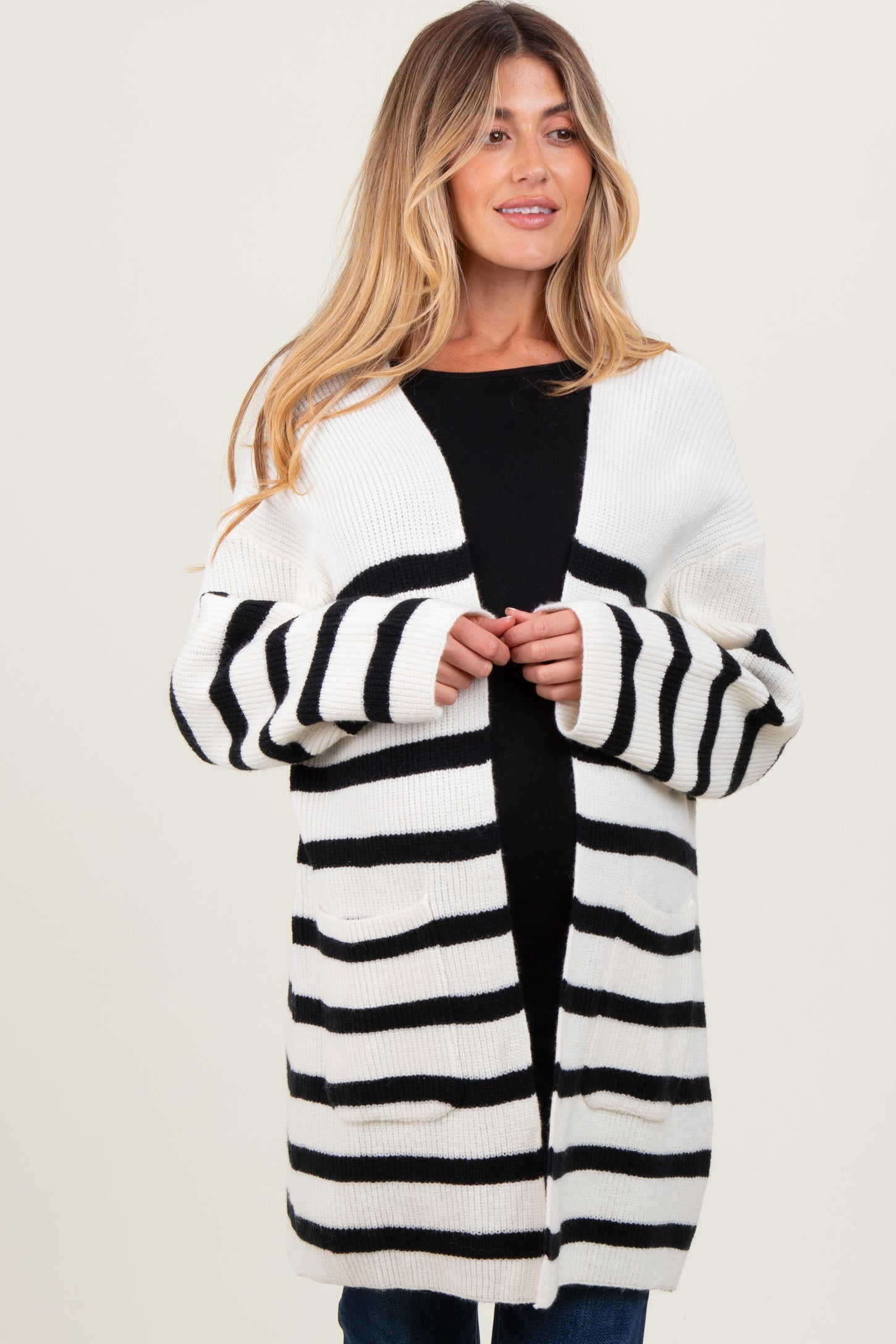 woman wearing a black and white striped maternity cardigan over a black top and holding her baby bump