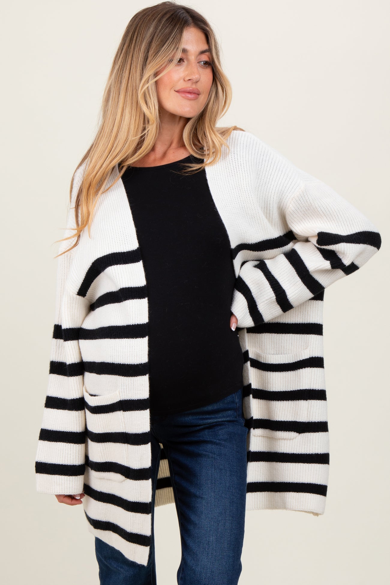 woman wearing a black and white striped maternity cardigan over a black top and showing a baby bump with dark jeans