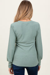 woman wearing a light green ribbed maternity top with puff sleeves, viewed from the back