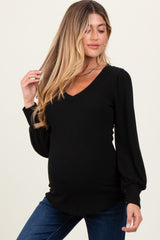 woman wearing a black ribbed maternity top with a v-neckline and puff sleeves, showing her baby bump
