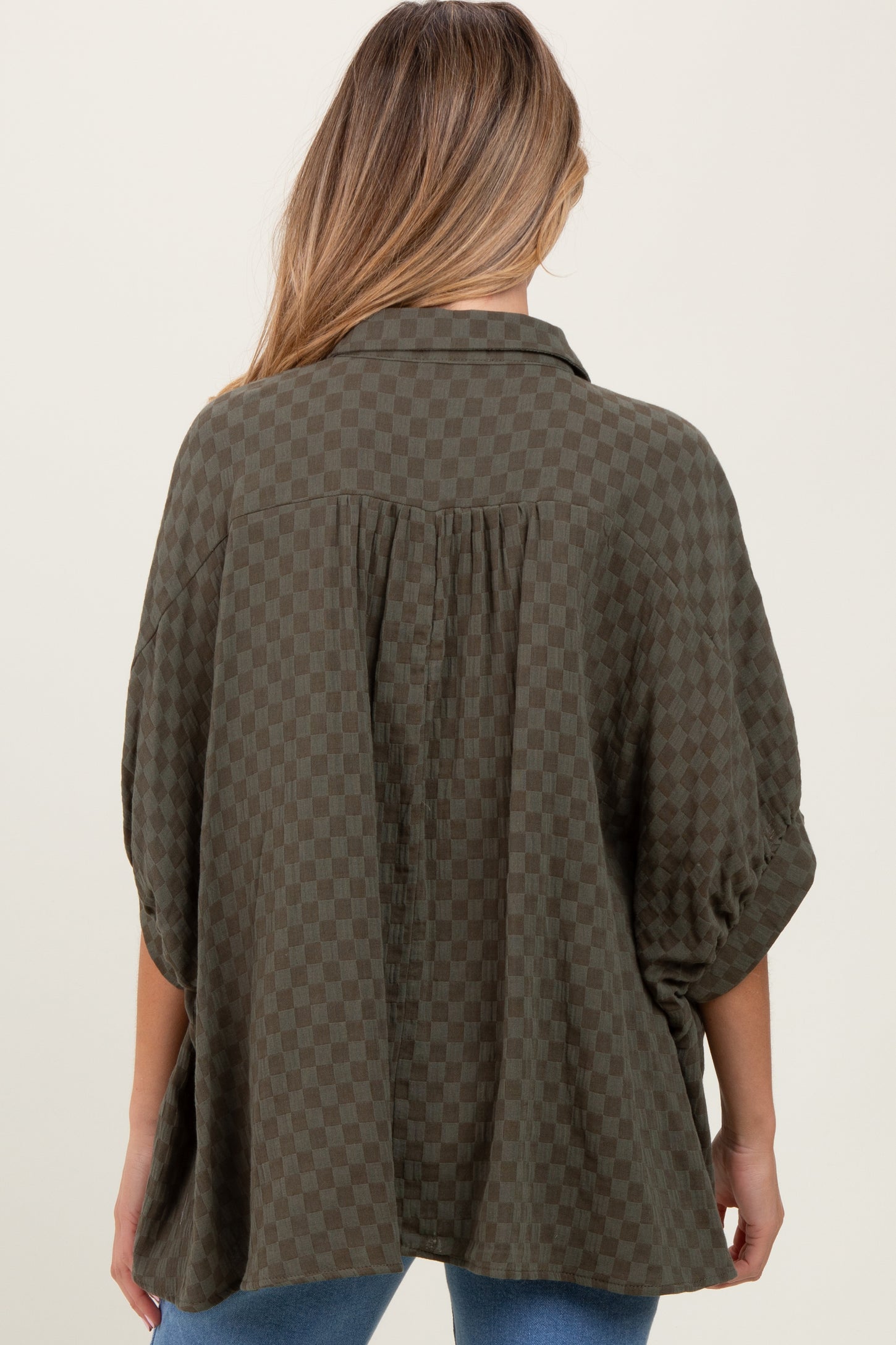 woman wearing a green checkered maternity button-up top with a relaxed fit and rolled sleeves, seen from the back
