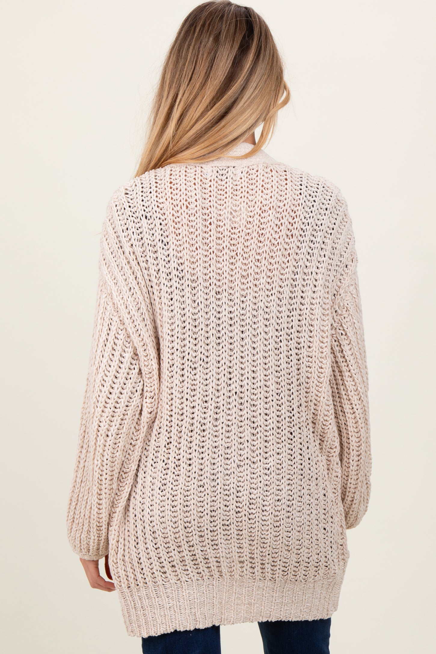 woman wearing a light beige loose knit maternity sweater viewed from the back