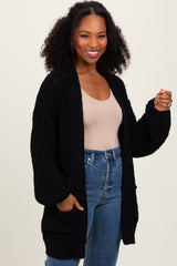 woman wearing a black oversized knit cardigan with pockets over a beige top and high-waisted jeans
