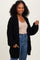 woman wearing a black oversized knit cardigan with pockets over a beige top and high-waisted jeans