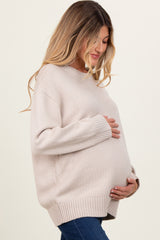 woman wearing a light beige oversized maternity sweater and cradling her baby bump