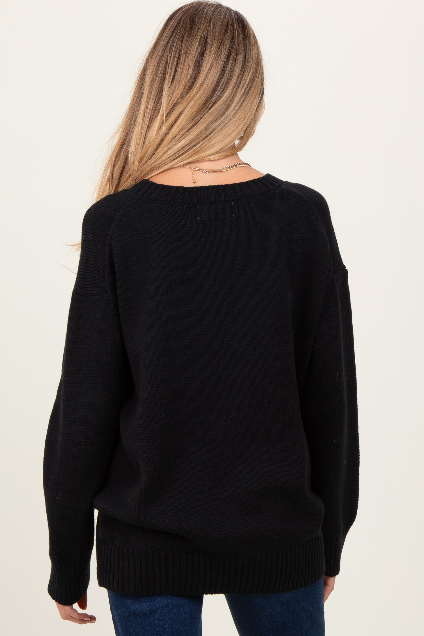 woman wearing a black oversized maternity sweater, seen from the back, showing relaxed fit and long sleeves