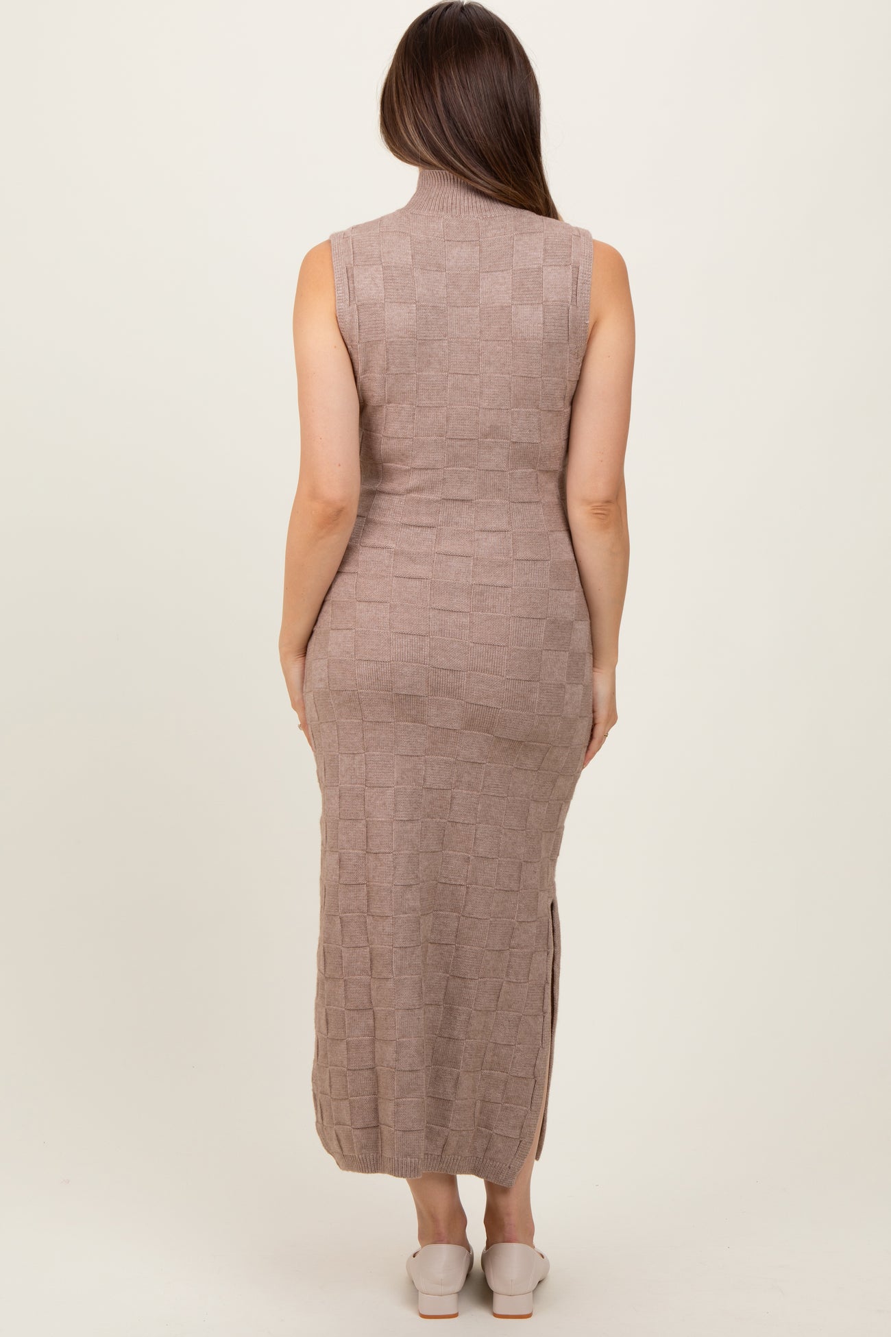 woman wearing a taupe sleeveless knitted maternity dress with a mock neck and side slits