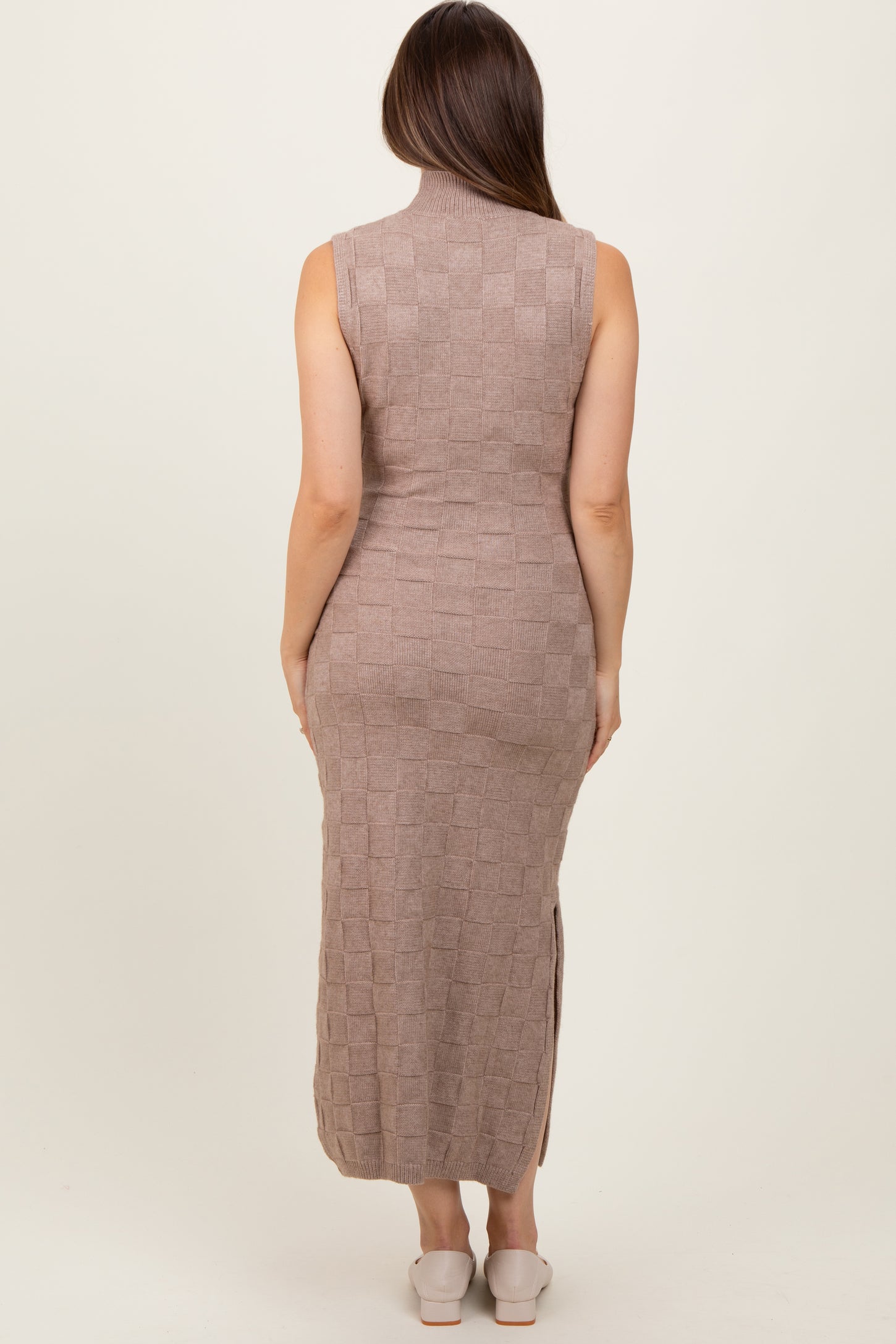 woman wearing a taupe sleeveless knitted maternity dress with a mock neck and side slits