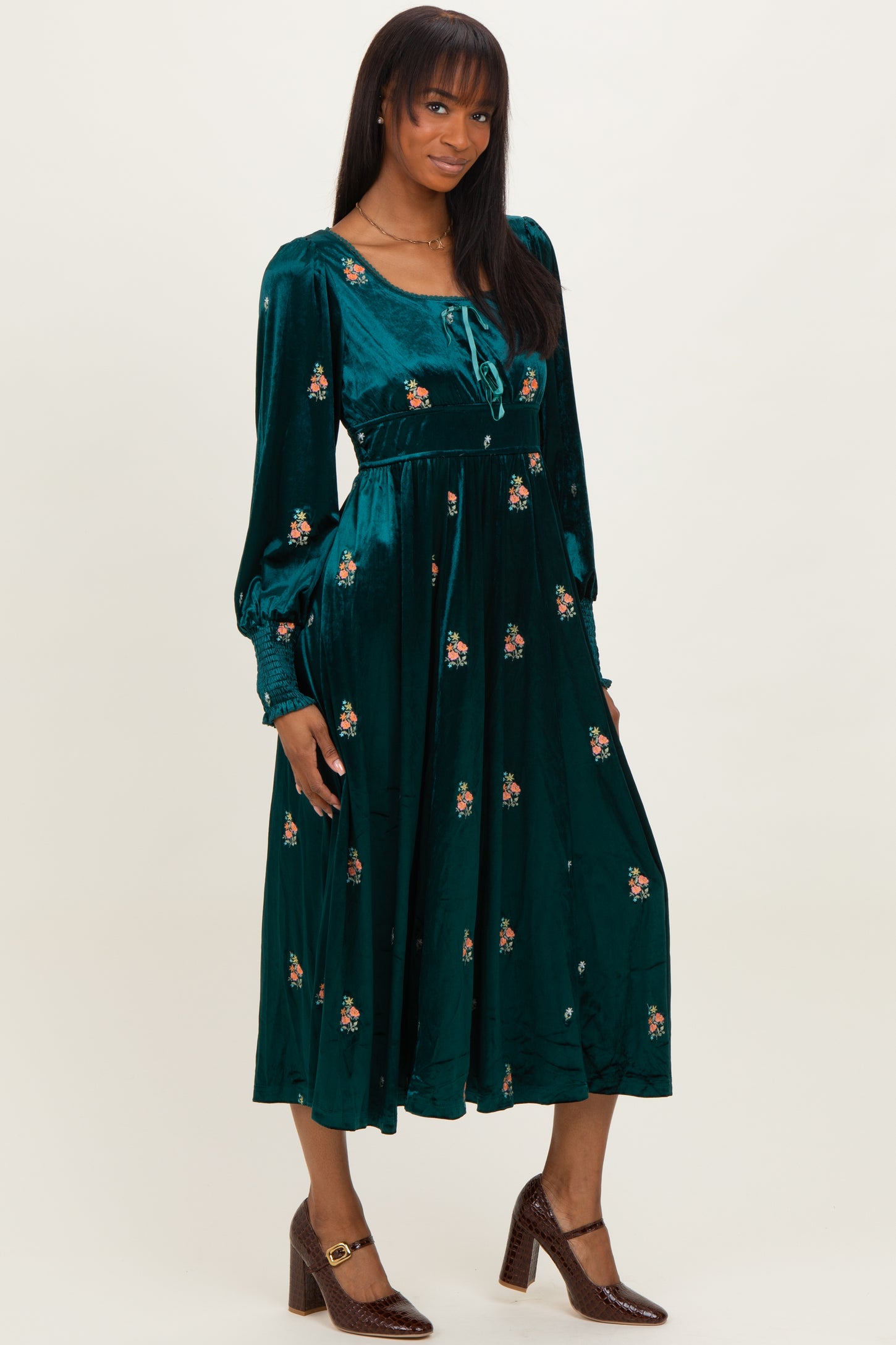 woman wearing a teal velvet floral midi dress with long sleeves and a tie neckline