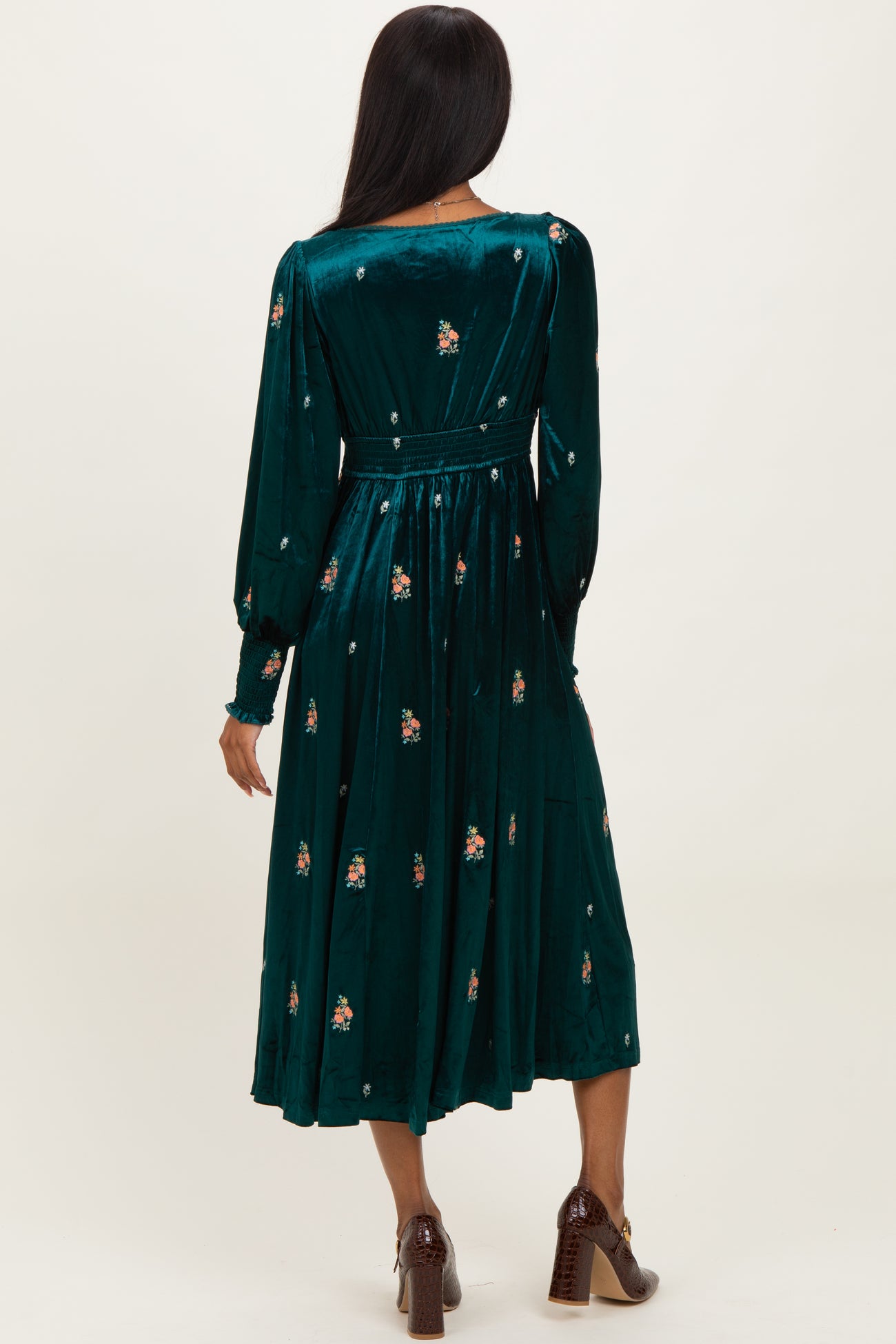 woman wearing a dark green velvet midi dress with floral embroidery and long sleeves, seen from the back