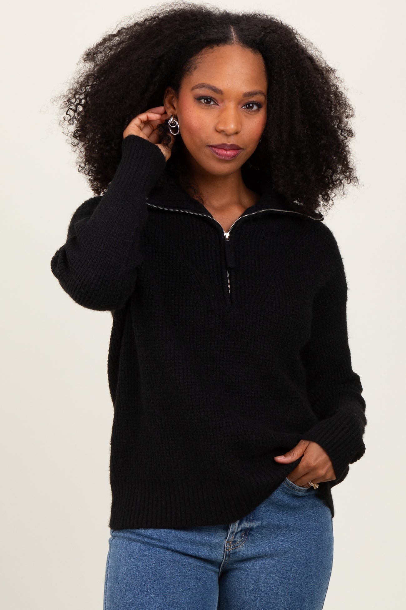 woman wearing a black zip-up sweater with a textured finish and blue jeans.