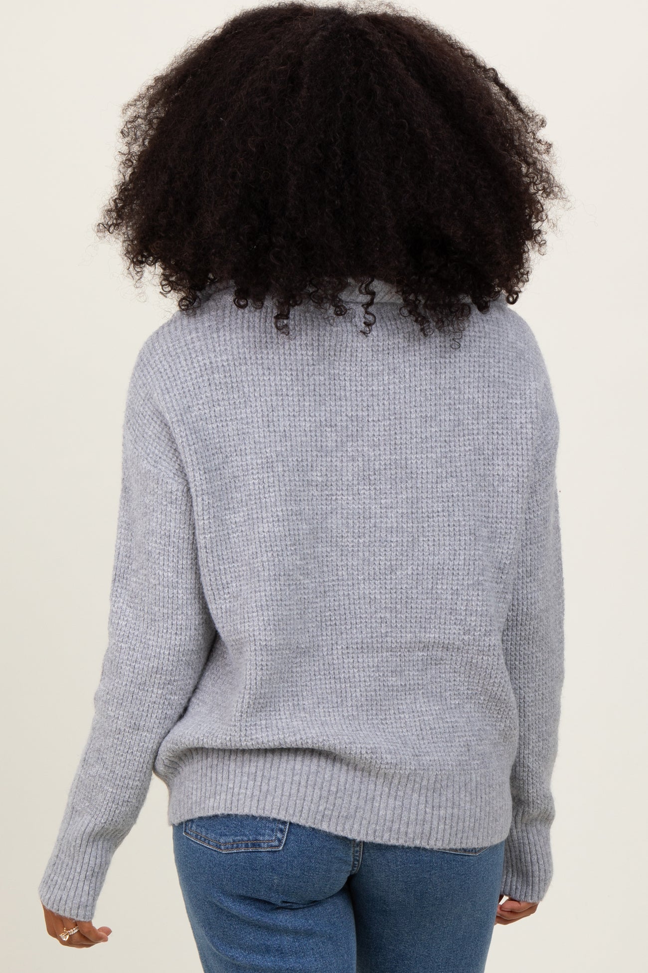 woman wearing a cozy gray knitted sweater with a relaxed fit and ribbed hem, viewed from the back