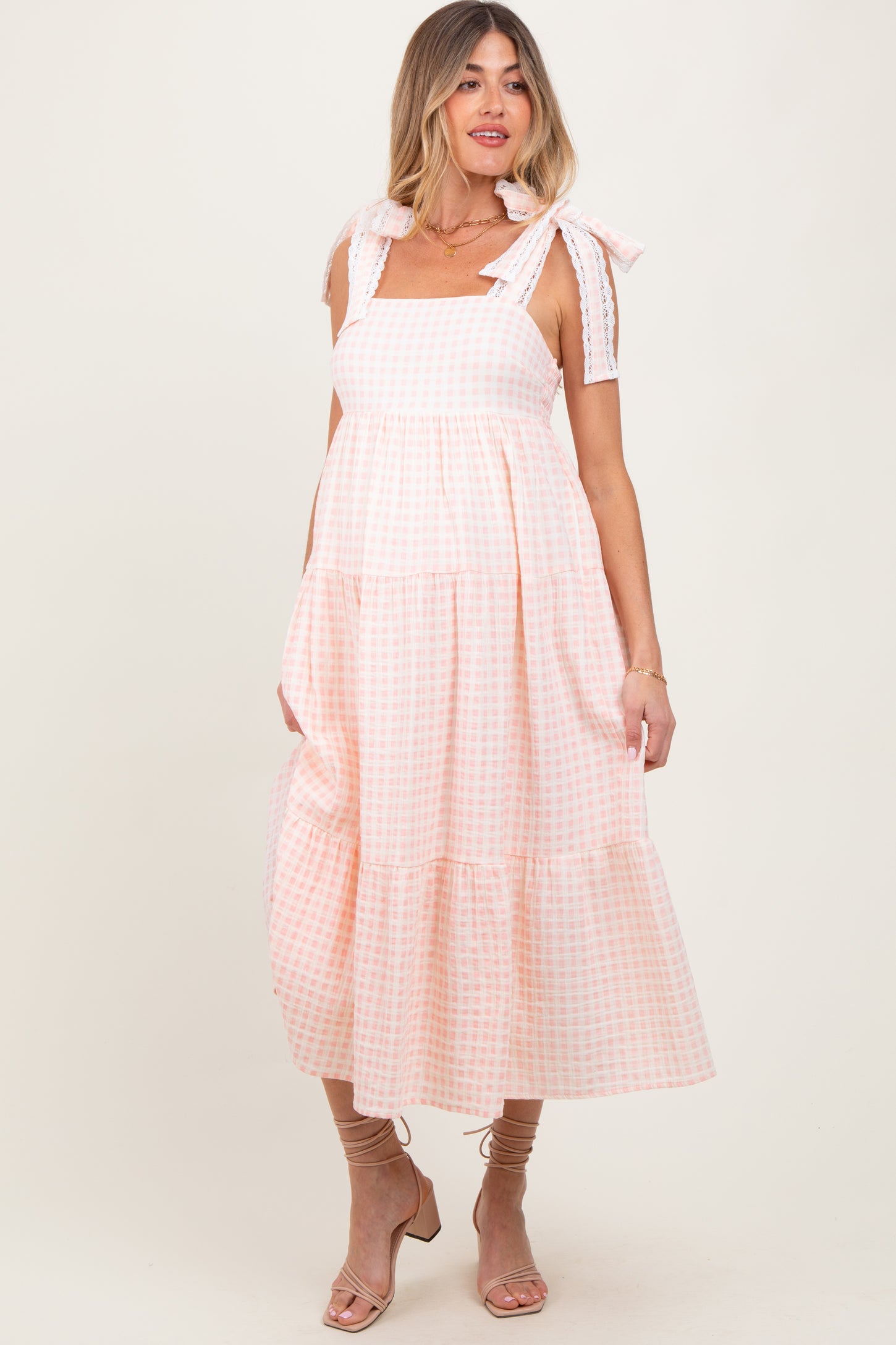 woman wearing a pink and white gingham maternity dress with tie straps and a tiered skirt, showcasing her baby bump