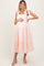 woman wearing a pink and white gingham maternity dress with tie straps and tiered skirt, holding her baby bump