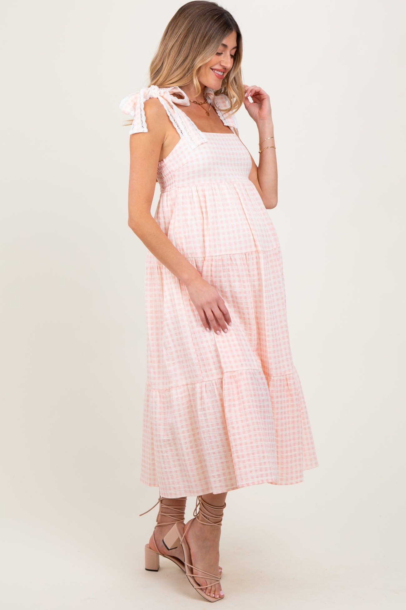 woman wearing a pink and white gingham maternity dress with tie straps and a flowing silhouette, showing baby bump