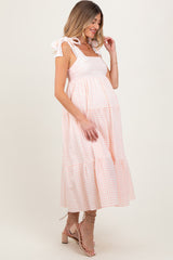 woman wearing a pink and white gingham maternity dress with tie straps and a flowing silhouette, showing baby bump