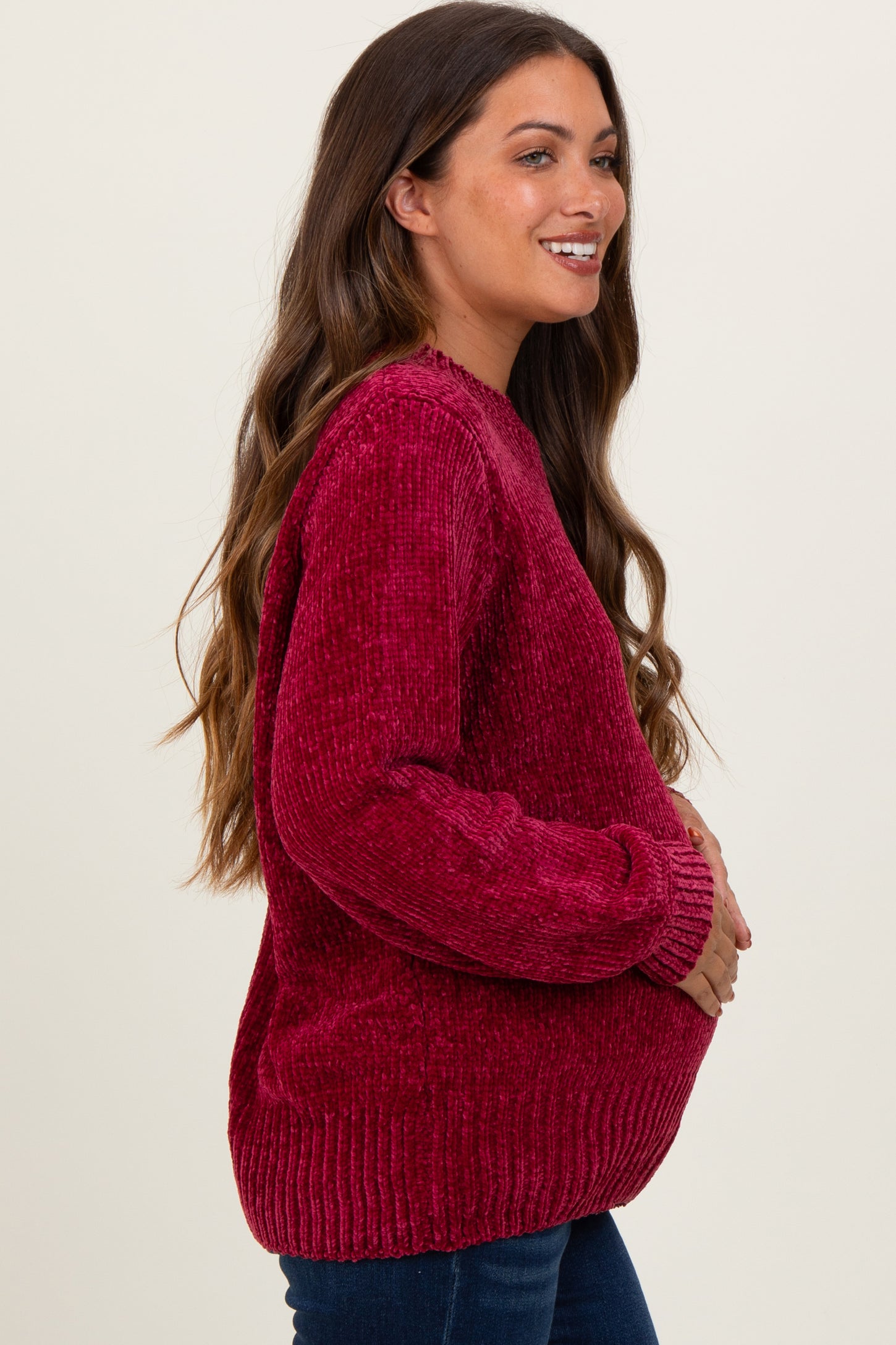 woman wearing a vibrant red maternity sweater, smiling and holding her baby bump, with long wavy hair