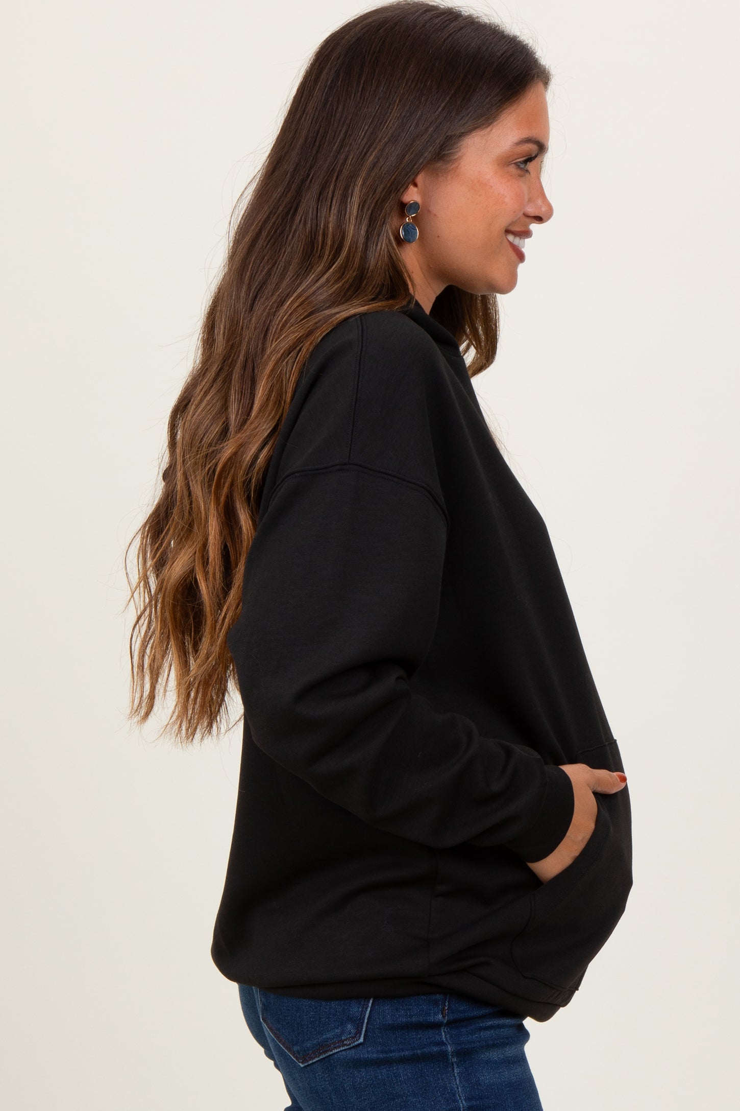 woman wearing a black oversized maternity sweatshirt with a side pocket and a visible baby bump