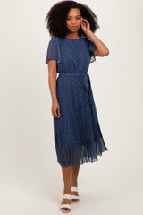 woman wearing a navy blue floral midi dress with short sleeves and a waist tie, standing against a neutral background