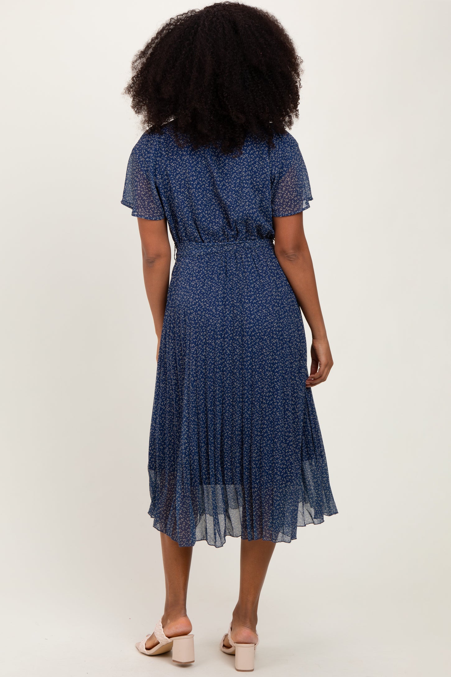 woman wearing a navy blue floral pleated midi dress with short sleeves, viewed from the back