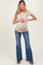 woman wearing a beige short sleeve maternity top and blue flared jeans, holding her baby bump