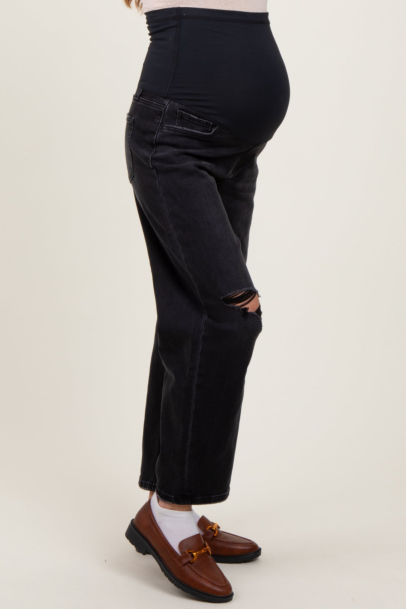 woman wearing black ripped maternity jeans with a supportive belly panel and brown loafers, showing her baby bump
