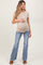 woman wearing a beige short sleeve maternity top and blue flared jeans, showing her baby bump