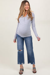 woman wearing a gray long sleeve maternity top and distressed blue maternity jeans, showing her baby bump