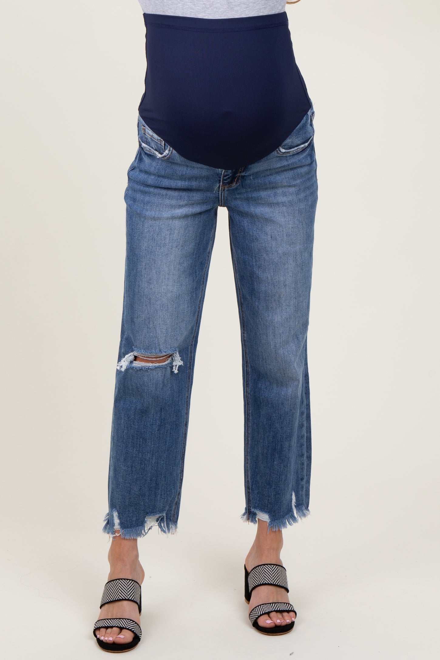 woman wearing a pair of distressed blue maternity jeans with a navy over-the-bump waistband