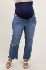 woman wearing a navy maternity wear top with light blue distressed maternity jeans and white heeled sandals, showcasing a baby bump