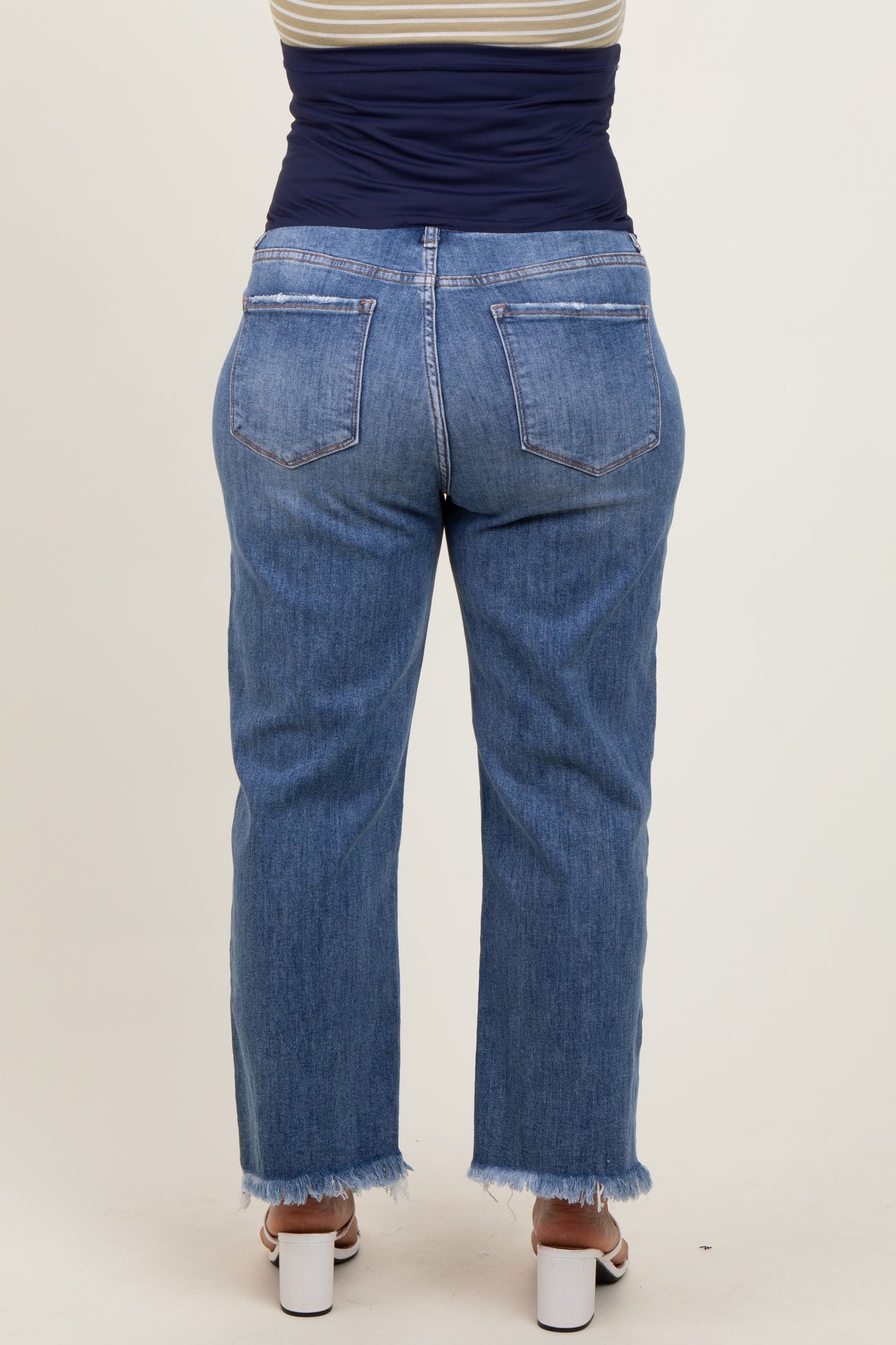 woman wearing a pair of light blue maternity plus size jeans with a frayed hem, viewed from the back