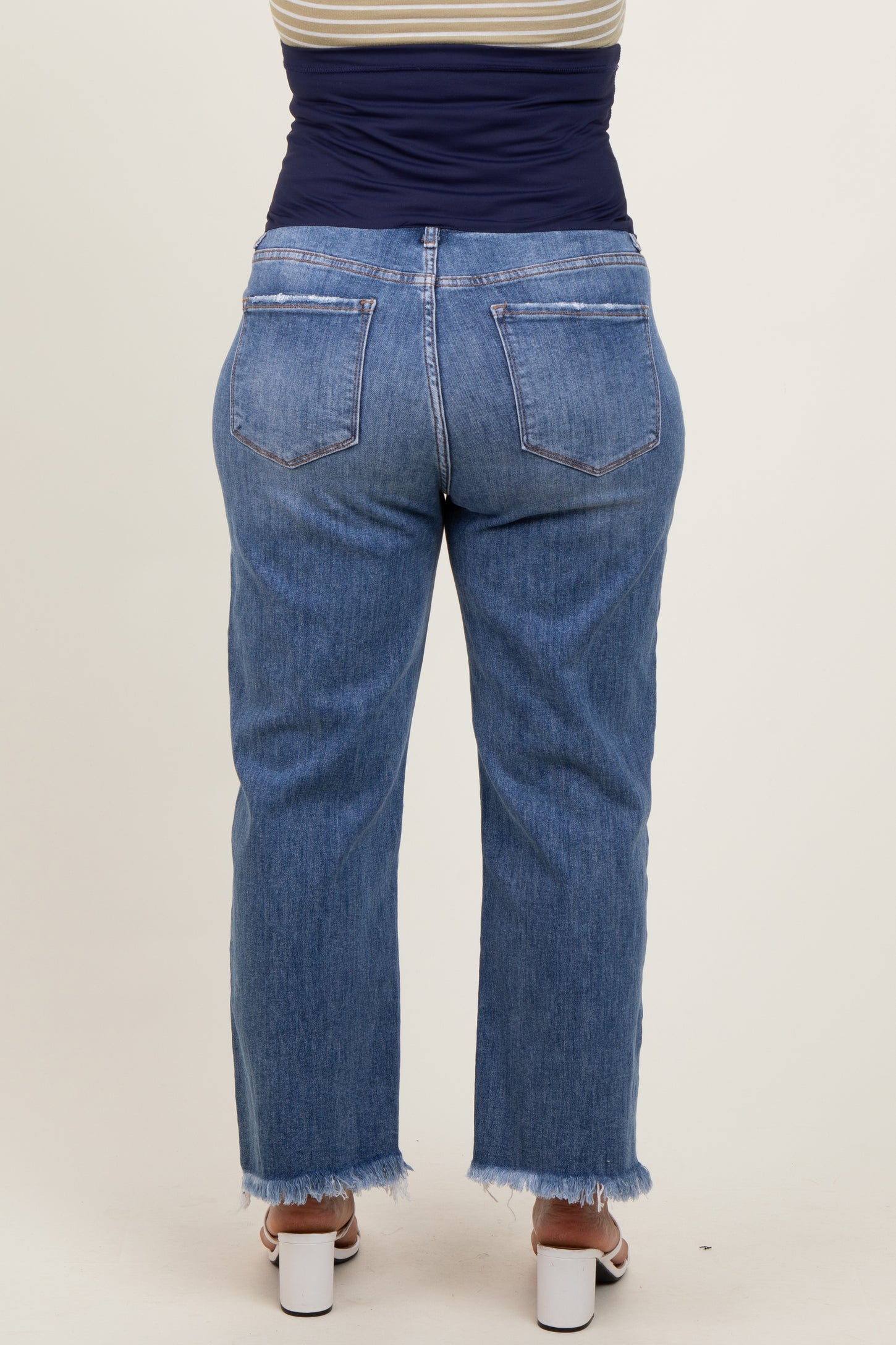 woman wearing a pair of light blue maternity plus size jeans with a frayed hem, viewed from the back