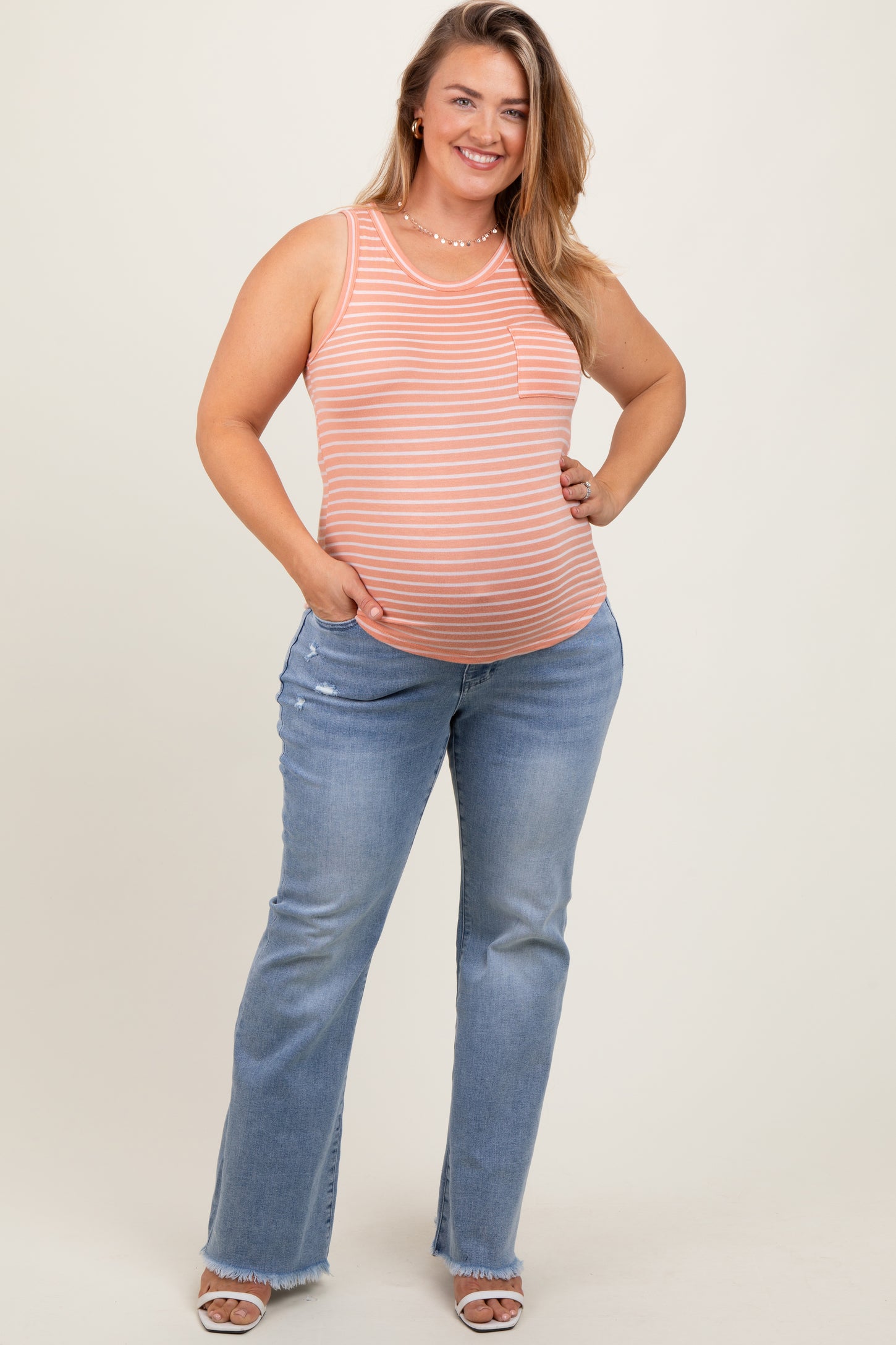 woman wearing a striped orange maternity tank top with a baby bump and flared light blue maternity jeans