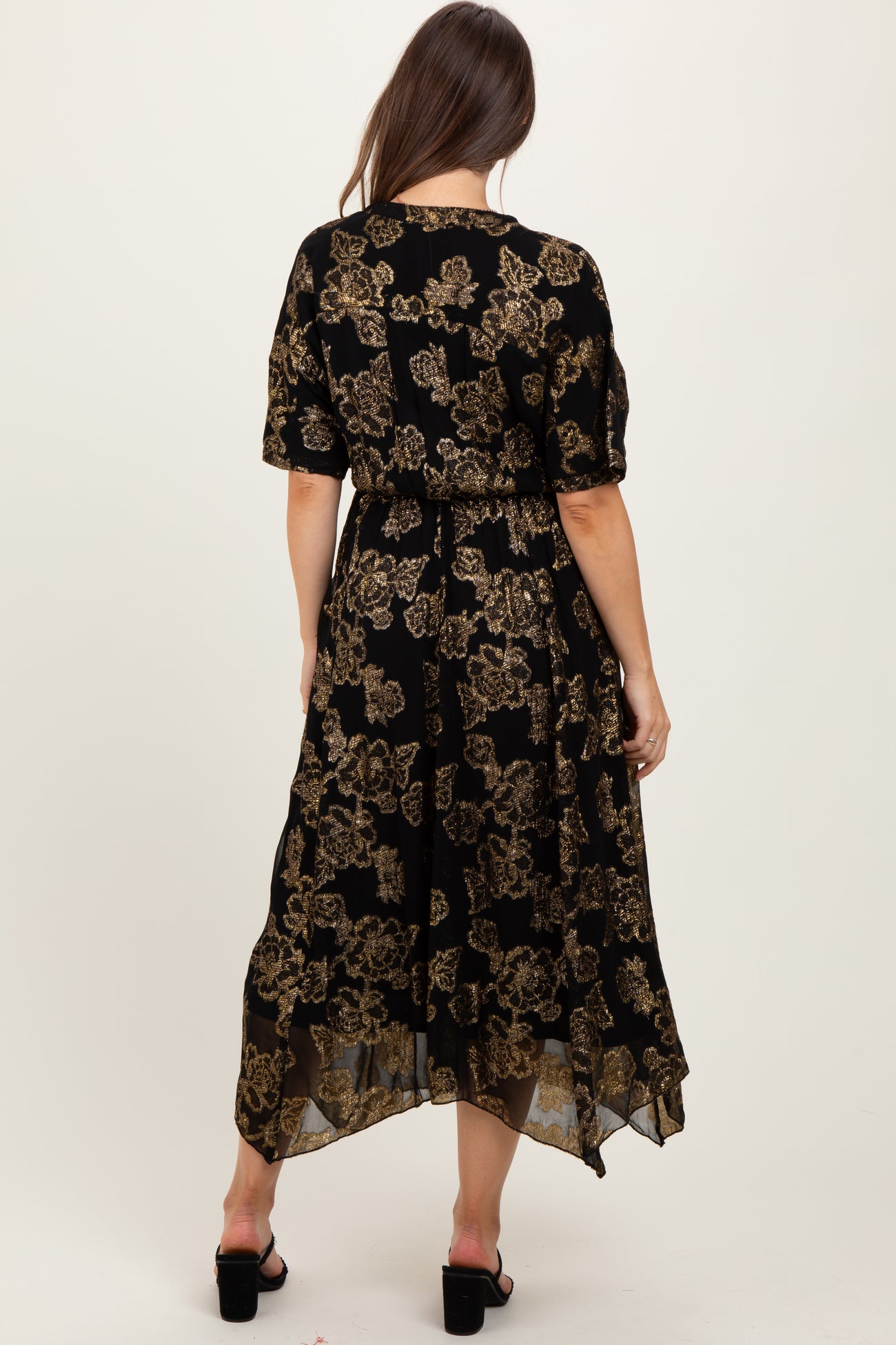woman wearing a black floral maternity dress with gold details, featuring short sleeves and a high-low hemline
