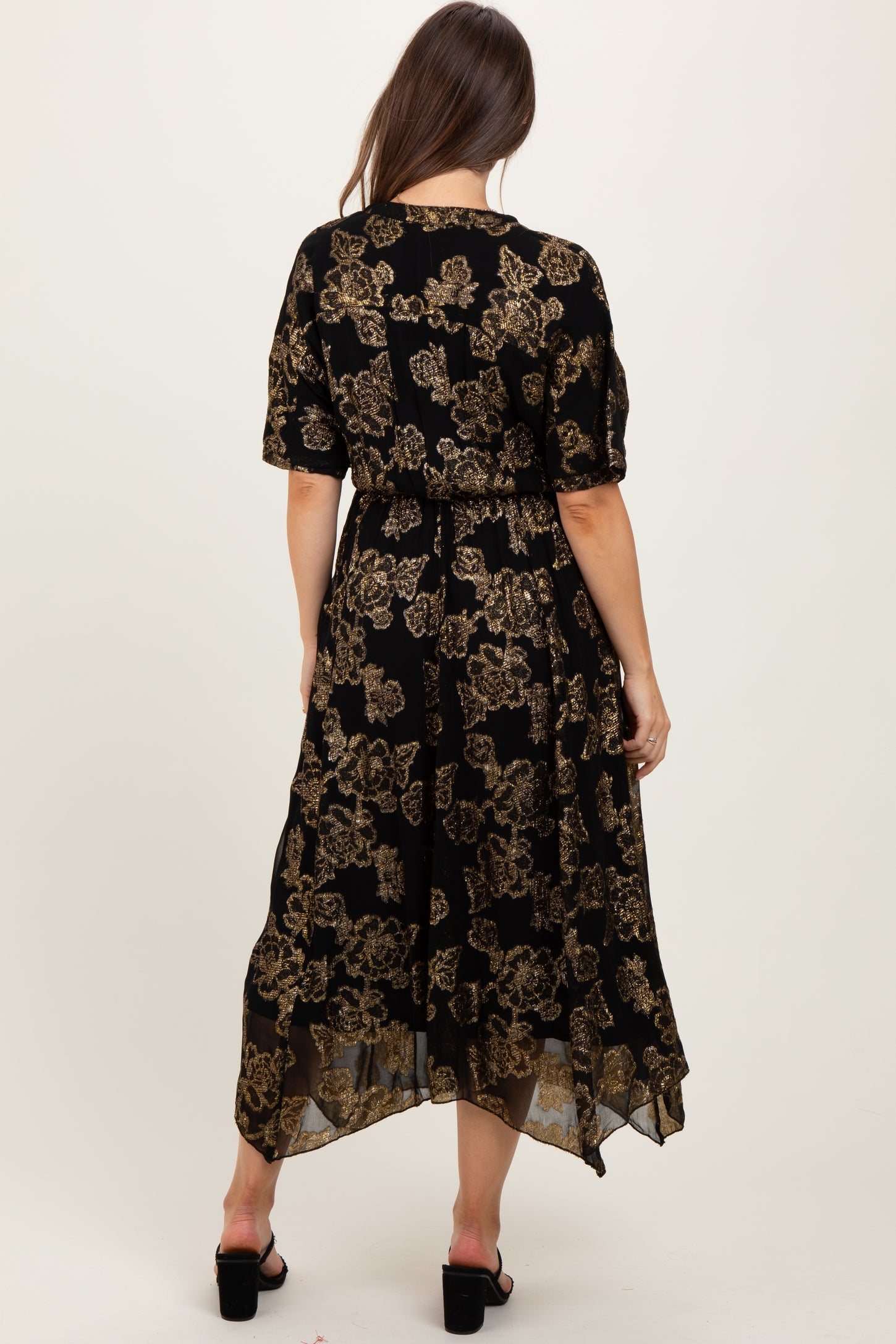 woman wearing a black floral maternity dress with gold details, featuring short sleeves and a high-low hemline