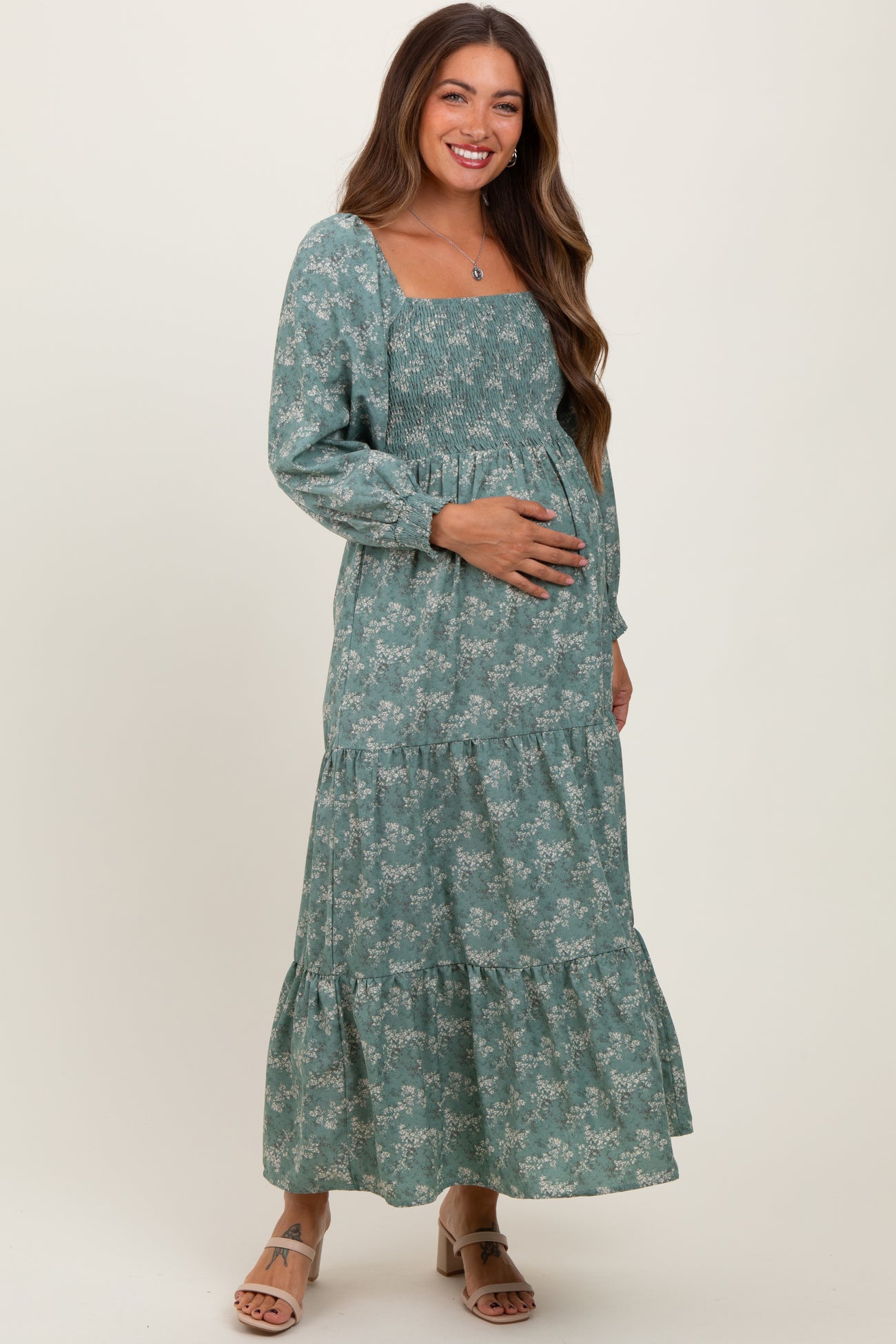 woman wearing a teal floral maternity maxi dress with smocked bodice and tiered skirt, holding her baby bump