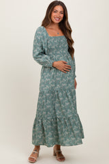 woman wearing a teal floral maternity maxi dress with smocked bodice and tiered skirt, holding her baby bump