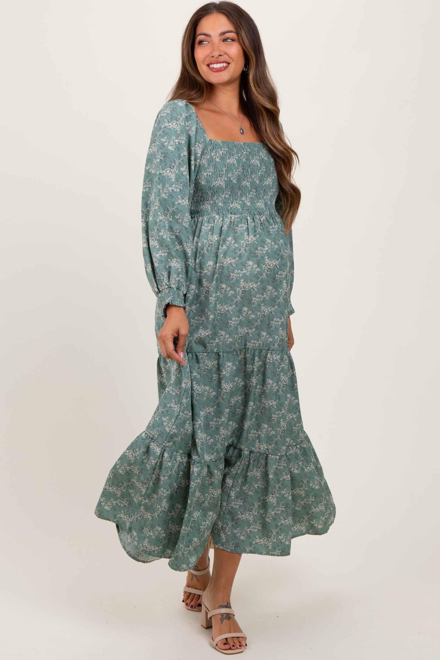 woman wearing a green floral maternity dress with a square neckline and tiered skirt, showcasing her baby bump
