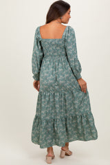 woman wearing a green floral maternity maxi dress with smocked bodice and puff sleeves, showing her baby bump